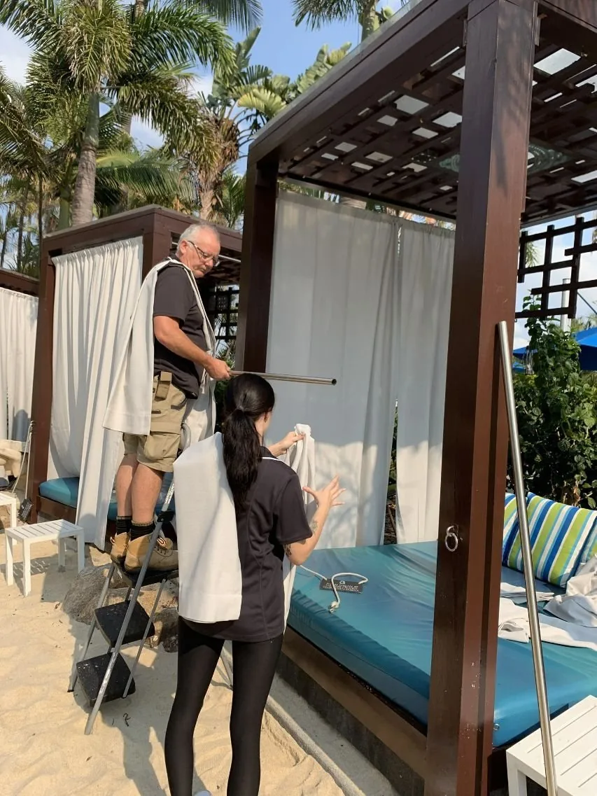 Two installers fitting outdoor curtains to a timber pergola