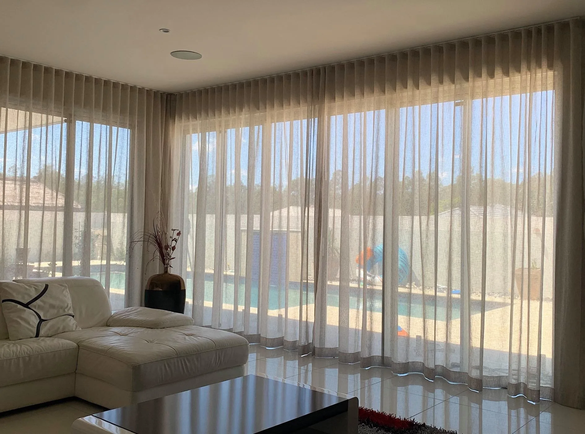 Sheer curtains drawn across a wide living room window overlooking a Brisbane pool and garden